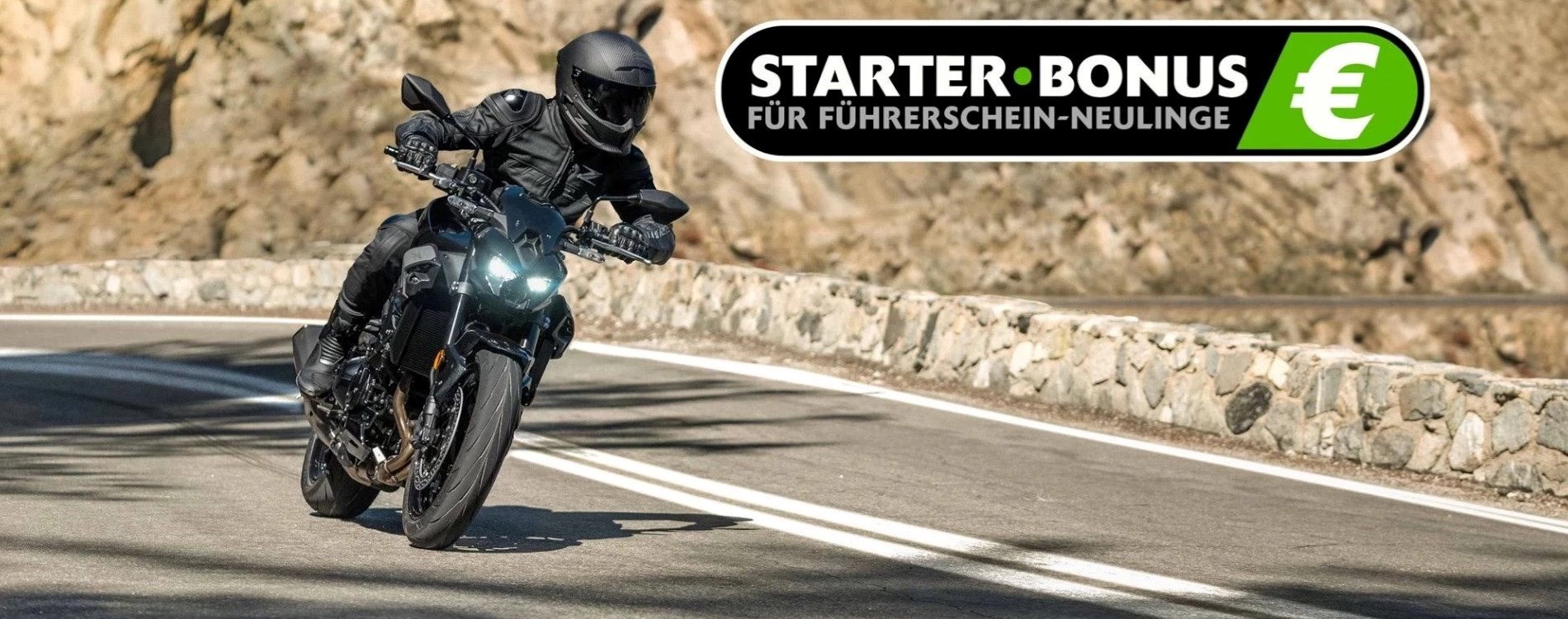 Das Bild zeigt einen Motorradfahrer in schwarzer Schutzkleidung und Helm auf der neuen Kawasaki Z900, der auf einer kurvigen Landstraße fährt. Rechts im Bild steht der Text „STARTER BONUS FÜR FÜHRERSCHEIN-NEULINGE“ als Logo. Der Hintergrund besteht aus felsigem Gelände.