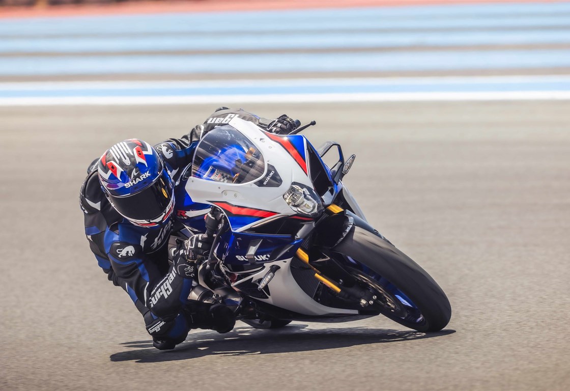 Fahrer in Rennmontur legt sich mit der neuen Suzuki GSX-R1000R 40th Anniversary Edition in weiß-blauer Sonderlackierung und Jubiläums-Emblem tief in die Kurve auf einer Rennstrecke
