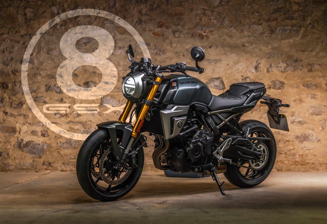Suzuki GSX-8S in mattgrüner Lackierung, ausgestellt vor einer rustikalen Steinwand. Das Naked Bike ist mit goldener Upside-Down-Gabel, rundem LED-Scheinwerfer und sportlichen Details ausgestattet. Im Hintergrund ist groß ein 8-Ball-Logo an der Wand zu sehen.