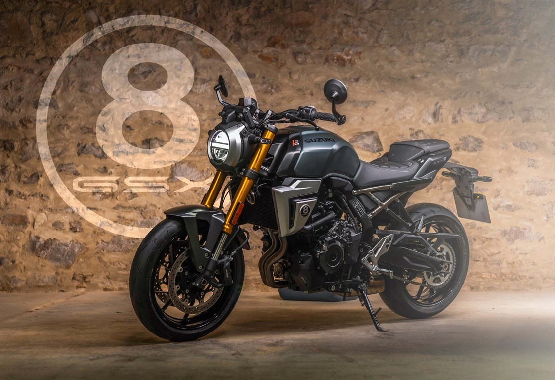 Suzuki GSX-8S in mattgrüner Lackierung, ausgestellt vor einer rustikalen Steinwand. Das Naked Bike ist mit goldener Upside-Down-Gabel, rundem LED-Scheinwerfer und sportlichen Details ausgestattet. Im Hintergrund ist groß ein 8-Ball-Logo an der Wand zu sehen.