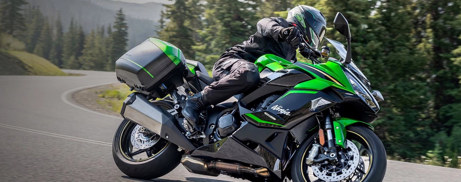 Das Bild zeigt eine Ninja 1100SX SE, ausgestattet mit einem Kofferset, fahrend auf der Landstraße.